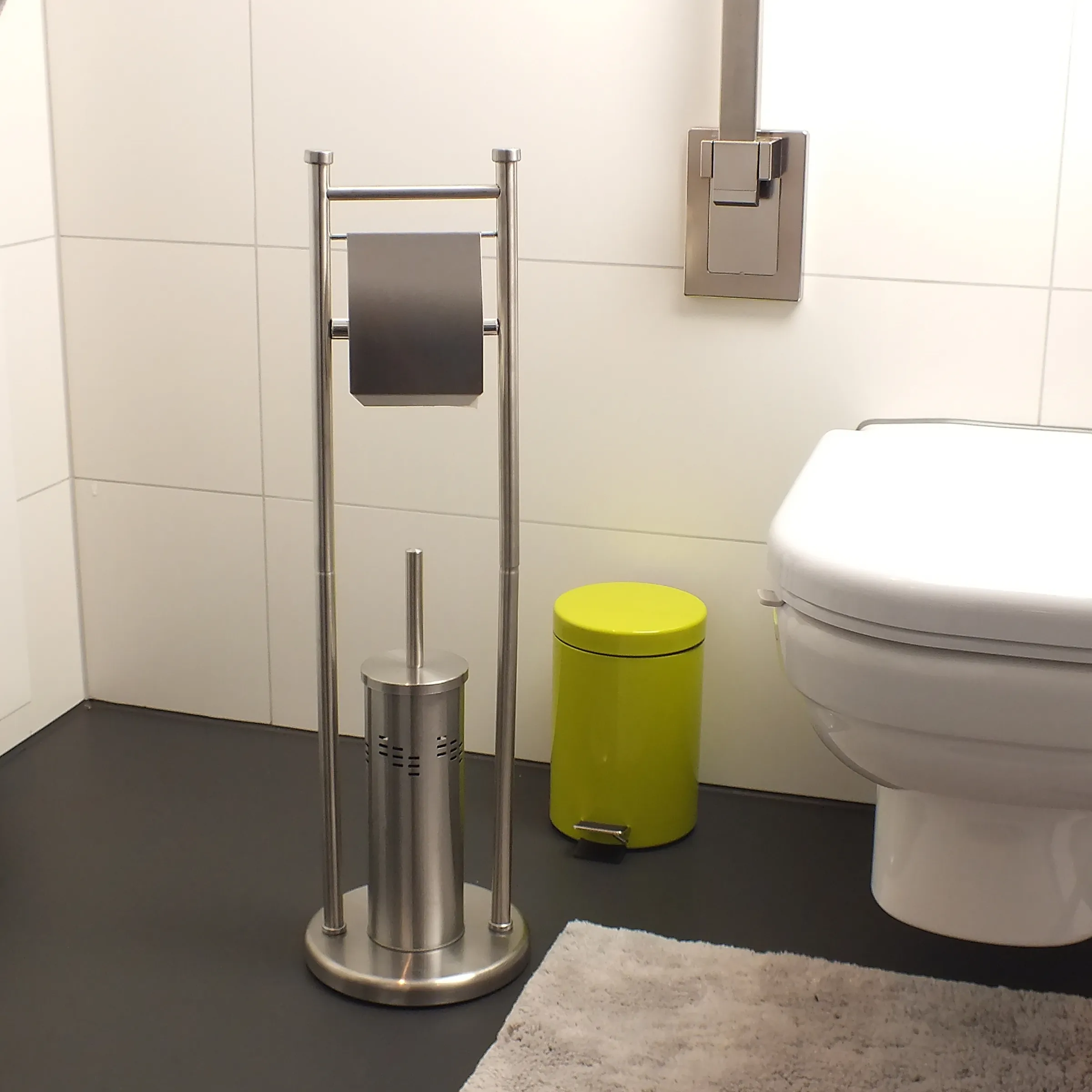 Modernes Badezimmer mit Edelstahl-Toilettenpapierhalter, grünem Tretmülleimer und Toilet-Bürste neben weißer Toilette