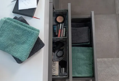 Schubladenorganizer Badezimmer Kosmetik und Handtücher Ordnungssystem mit grünen Handtüchern und Kosmetikprodukten in einer offenen Schublade mit Organizer