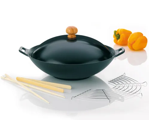 Wok-Set mit Deckel, Bambusstäbchen und Zubehör - Asiatische Küche Schwarzer Wok mit Deckel, Holzgriff, Bambusstäbchen und Metallrost, daneben gelbe Paprika auf weißem Hintergrund