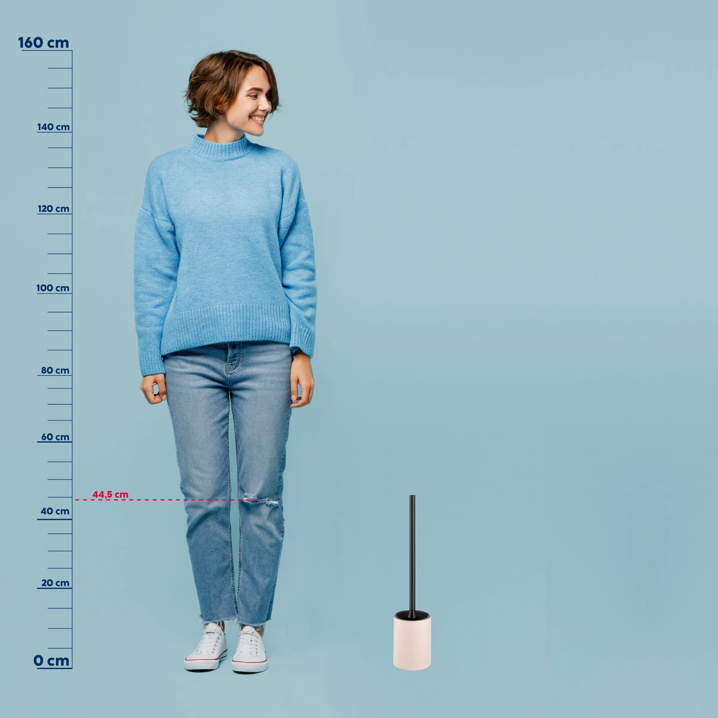 Frau in hellblauem Strickpullover und Jeans mit Größenvergleich einer Toilettenbürste, Höhenmarkierungen bis 160 cm
