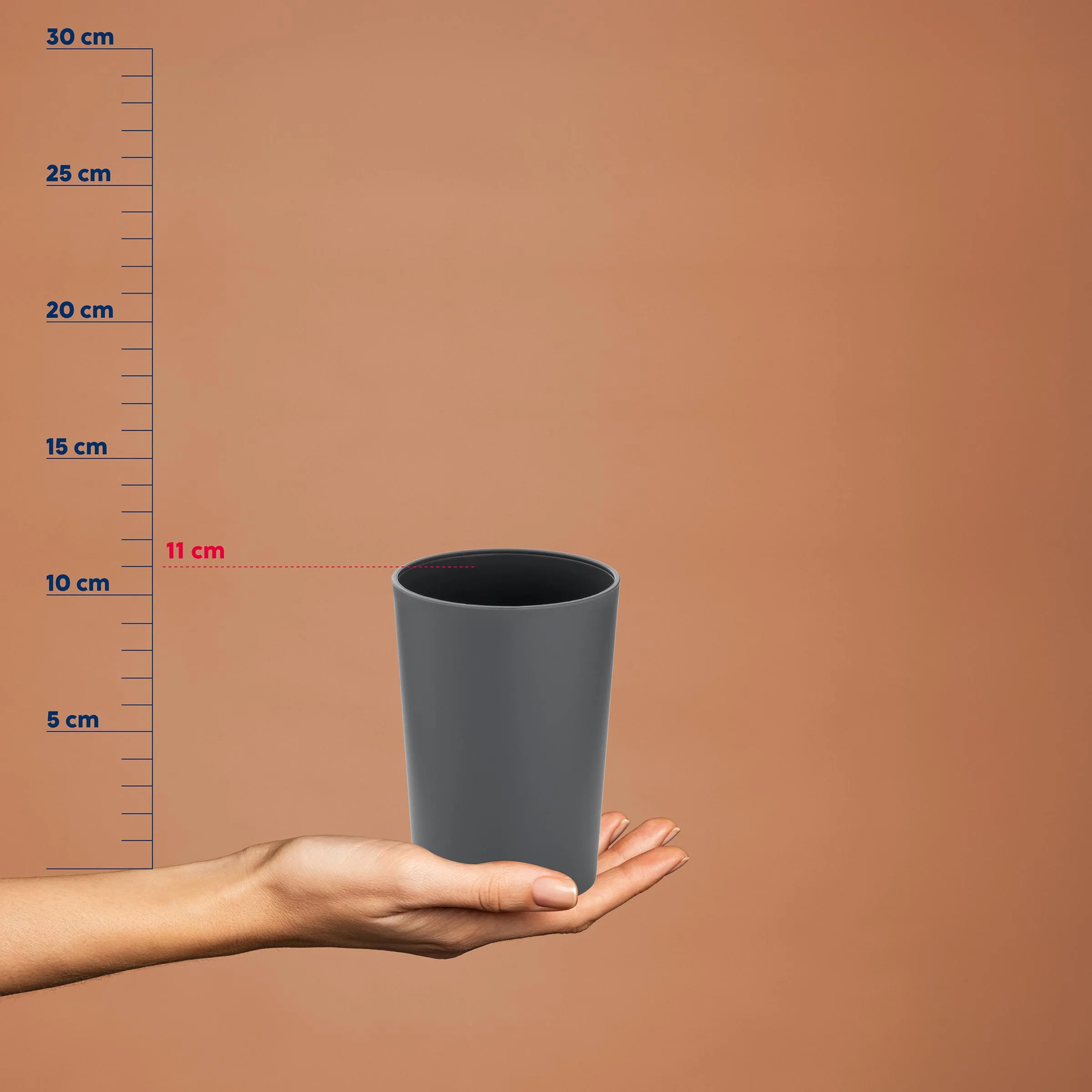 Hand hält grauen Kunststoffbecher vor Messskala, Höhe 11 cm, auf beigem Hintergrund