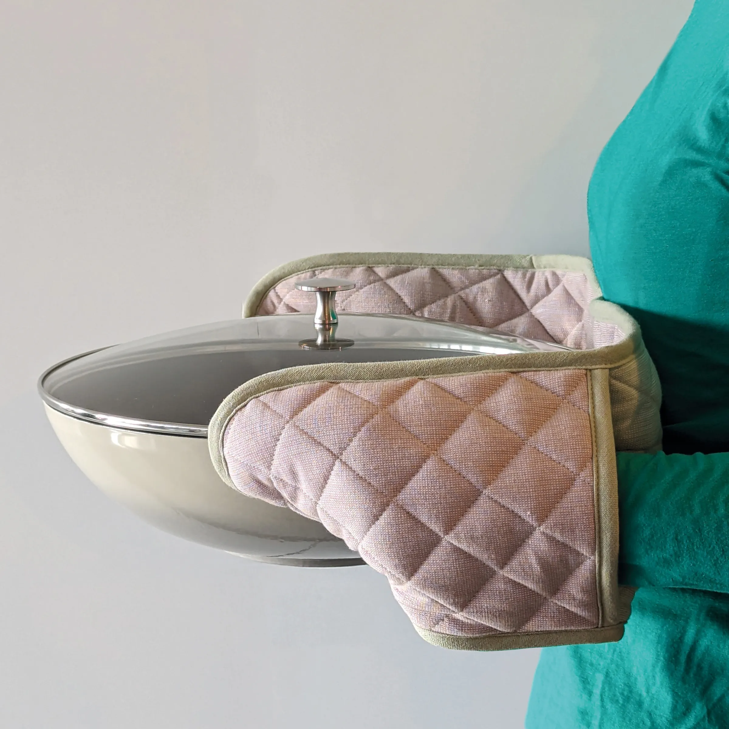 Topflappen Schutzhandschuhe Küche Kochabendteuer Person in türkisem Outfit trägt rosa Topflappen und hält einen Topf mit Glasdeckel