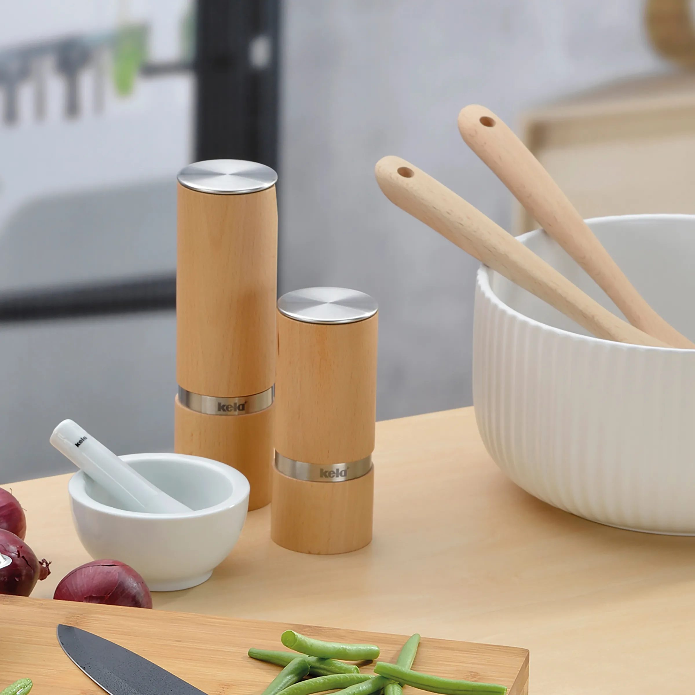 Küchenutensilien Set Holz Pfeffermühle Mörser Holzküchen-Set mit zwei Pfeffermühlen, Mörserstöße, weißer Schüssel und Holzlöffeln auf Arbeitstisch mit Gemüse