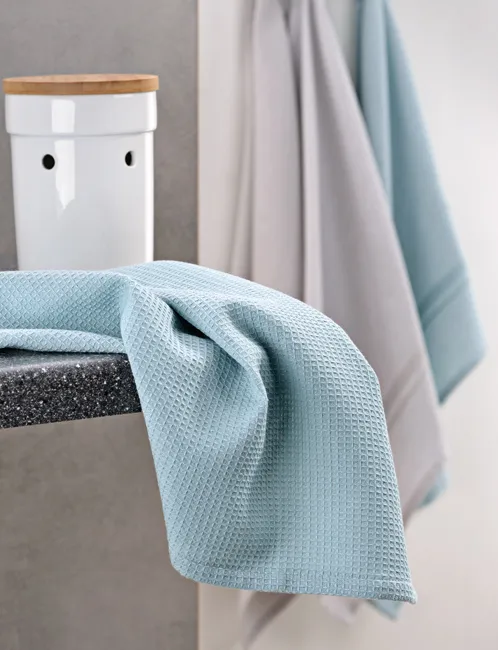 Baumwollhandtücher blau - Badezimmer Textilien Hellblaue Baumwollhandtücher hängen über einer Stange neben einem weißen Behälter mit Holzdeckel