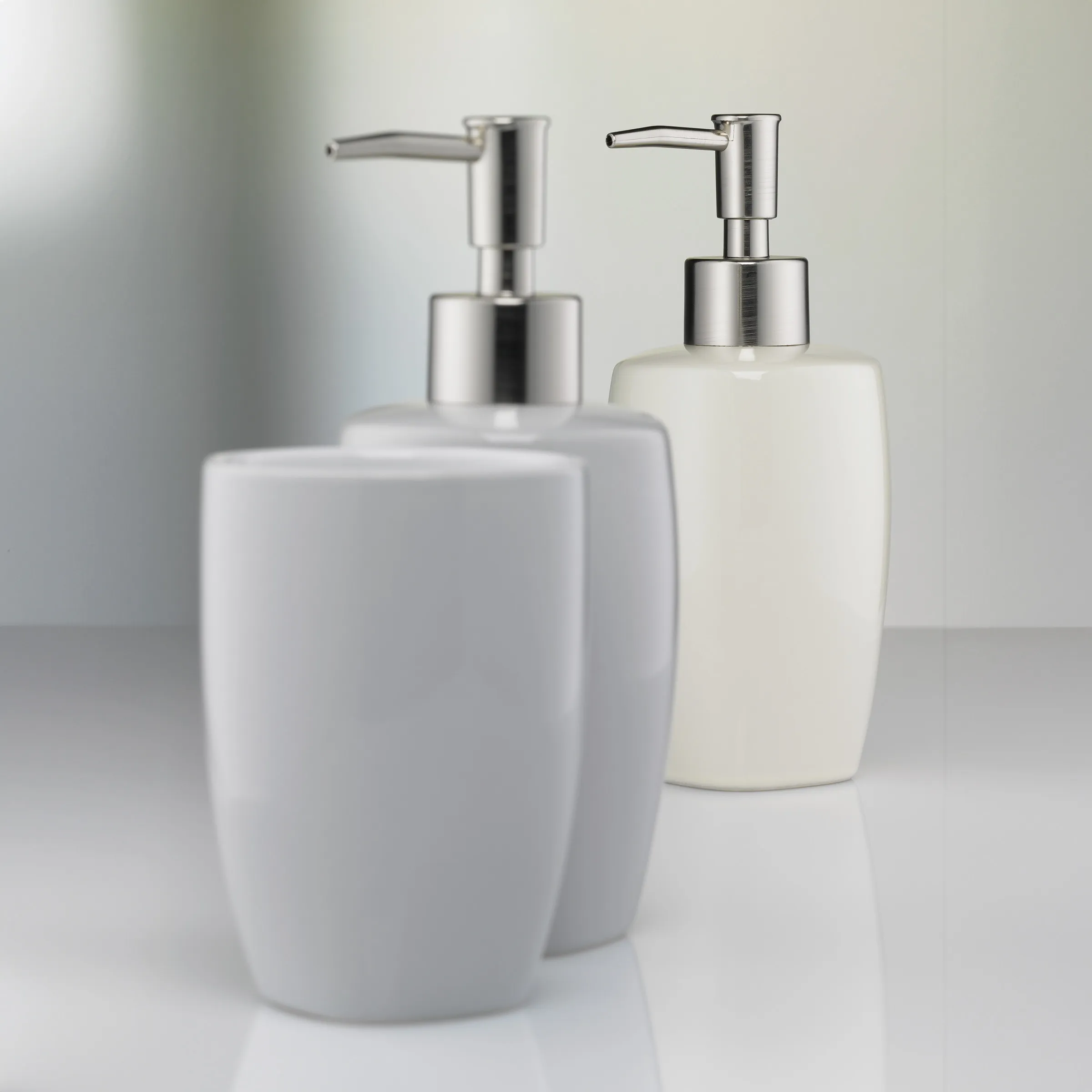 Seifenspender Set Weiß Keramik mit Edelstahl-Pumpe - Badezimmer Accessoires Zwei weiße Keramik-Seifenspender mit silbernen Edelstahlpumpen auf grauer Oberfläche vor hellem Hintergrund