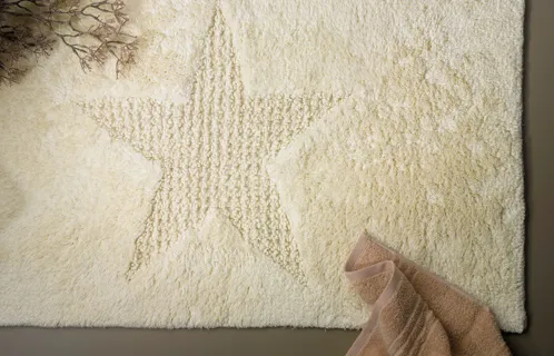 Badteppich mit Sternmuster - hochwertige Baumwolle Cremefarbener Badteppich mit Sternmuster, eine Hand deutet auf die strukturierte Oberfläche