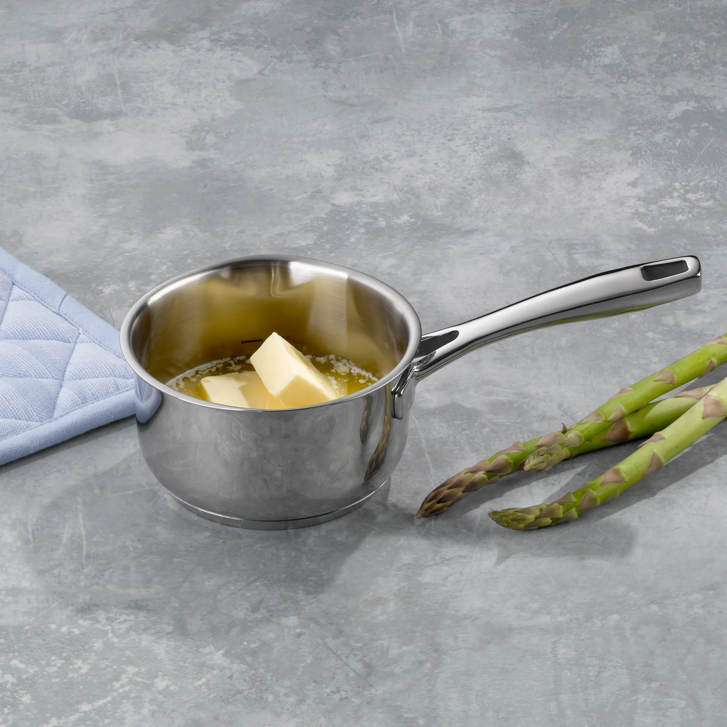 Edelstahl-Stieltopf mit Butter und Spargel - Kochtopf für die Küche Edelstahl-Stieltopf mit schmelzender Butter und Olivenöl neben frischem grünem Spargel auf grauer Arbeitsfläche