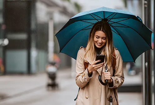 Lächelnde Frau mit blondem Haar hält einen dunkelblauen Regenschirm über sich in einer urbanen Straße
