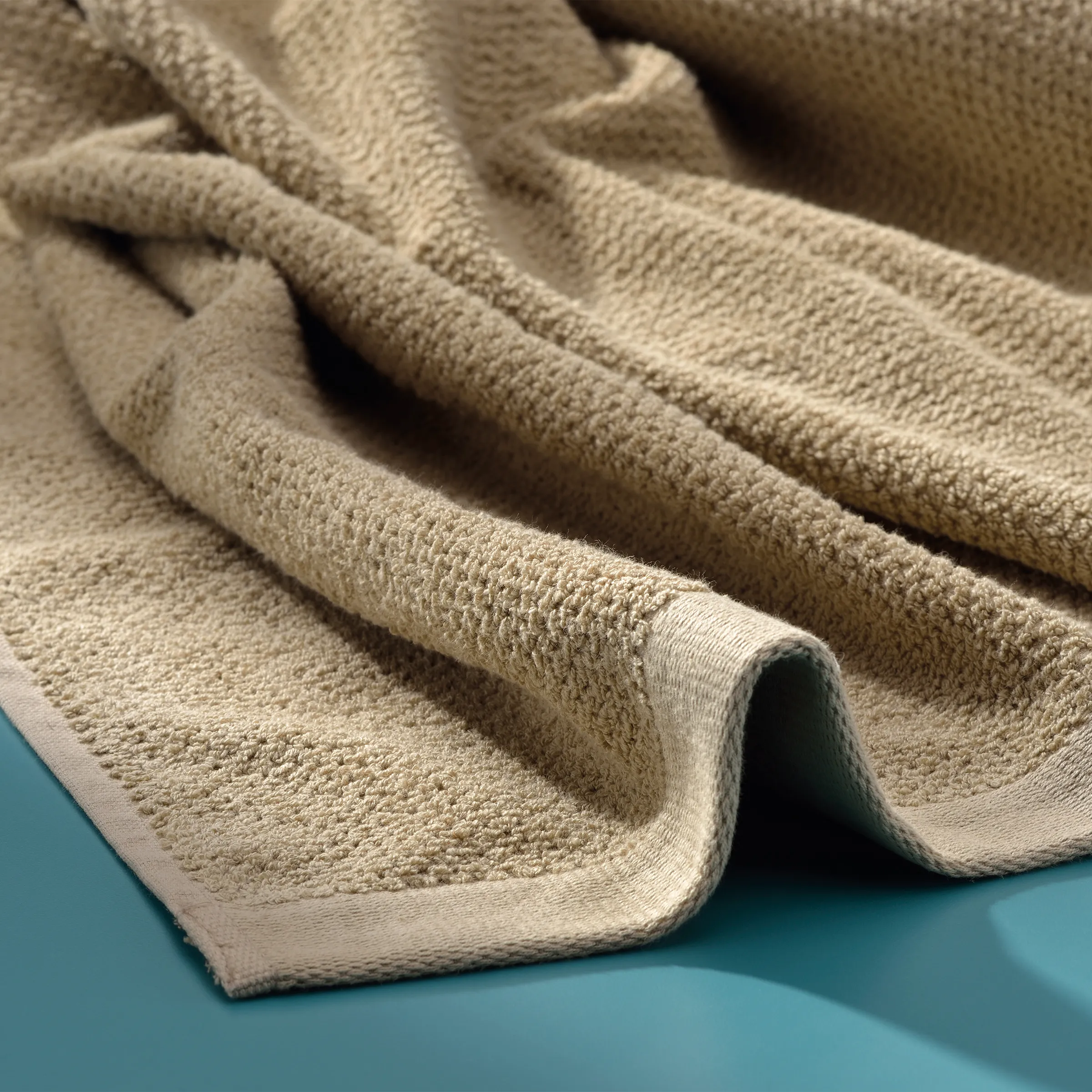 Weiche Frottee-Handtücher in Beige - Premium Baumwolle Beige Handtücher aus Frottee mit weicher Textur, gefaltet auf türkisfarbenem Untergrund