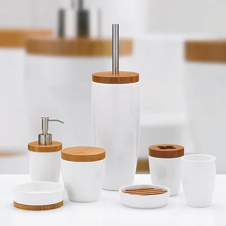 Badezimmer-Accessoires Set mit weißen Behältern und Bambusdeckeln, bestehend aus Seifenspender, Zahnbürstenhalter und Dosen.