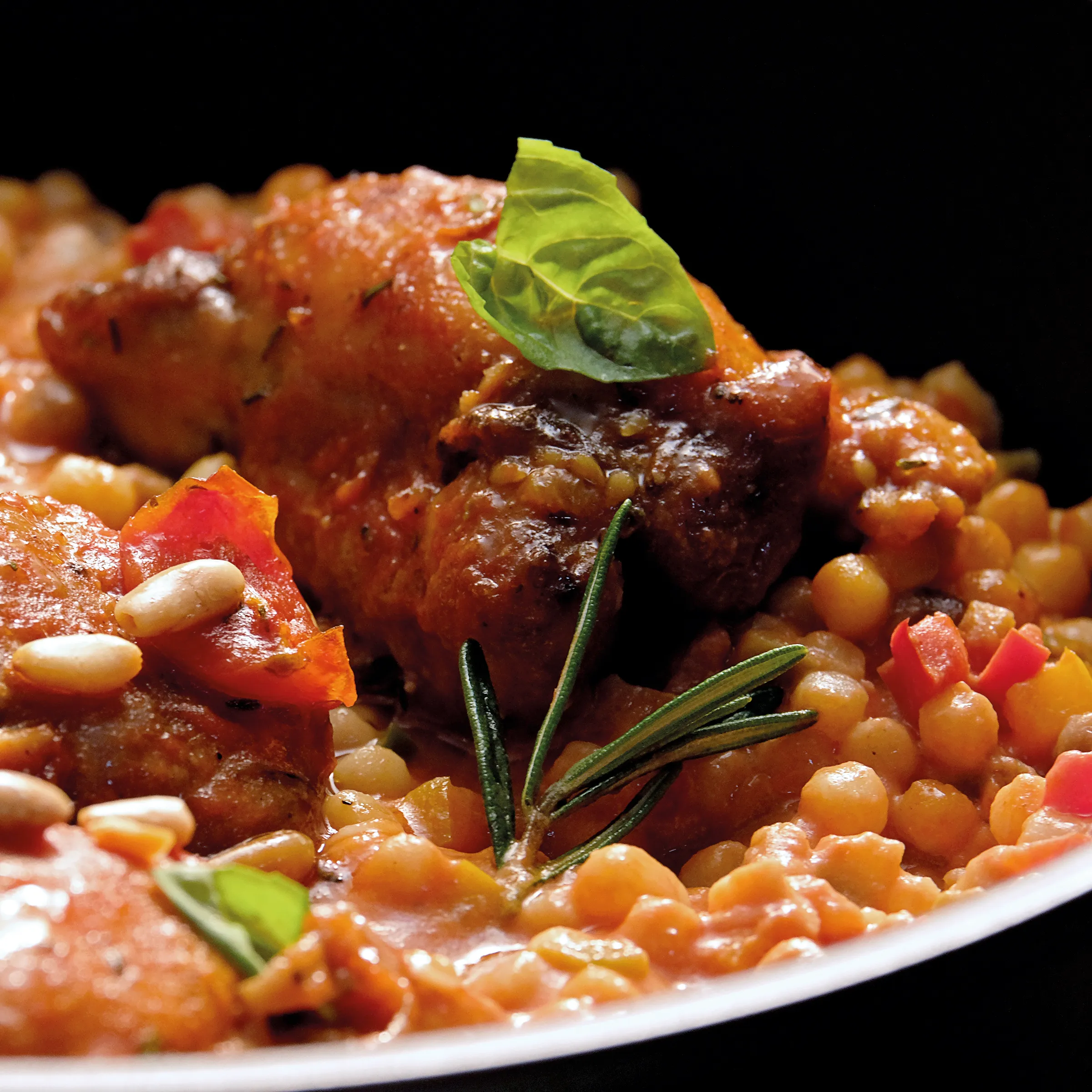 Eintopf Rezept: Schmorfleisch mit Kichererbsen und Gemüse Geschmortes Fleisch mit Kichererbsen, Paprika und Kräutern auf schwarzem Hintergrund garniert mit Rosmarin und Basilikum