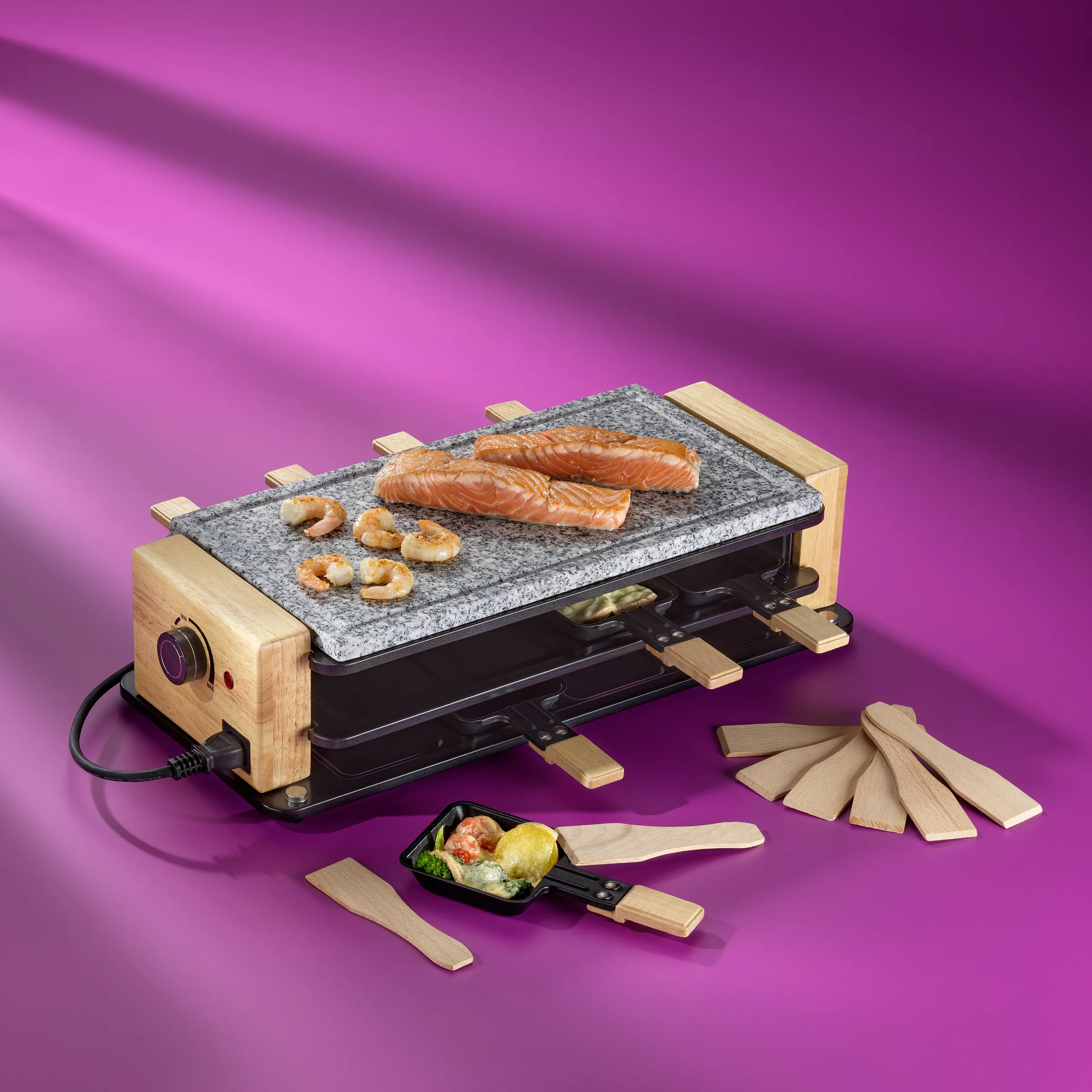 Raclette-Grill mit Holzelementen und Granitplatte, belegt mit Lachsfilets und Garnelen auf violettem Hintergrund