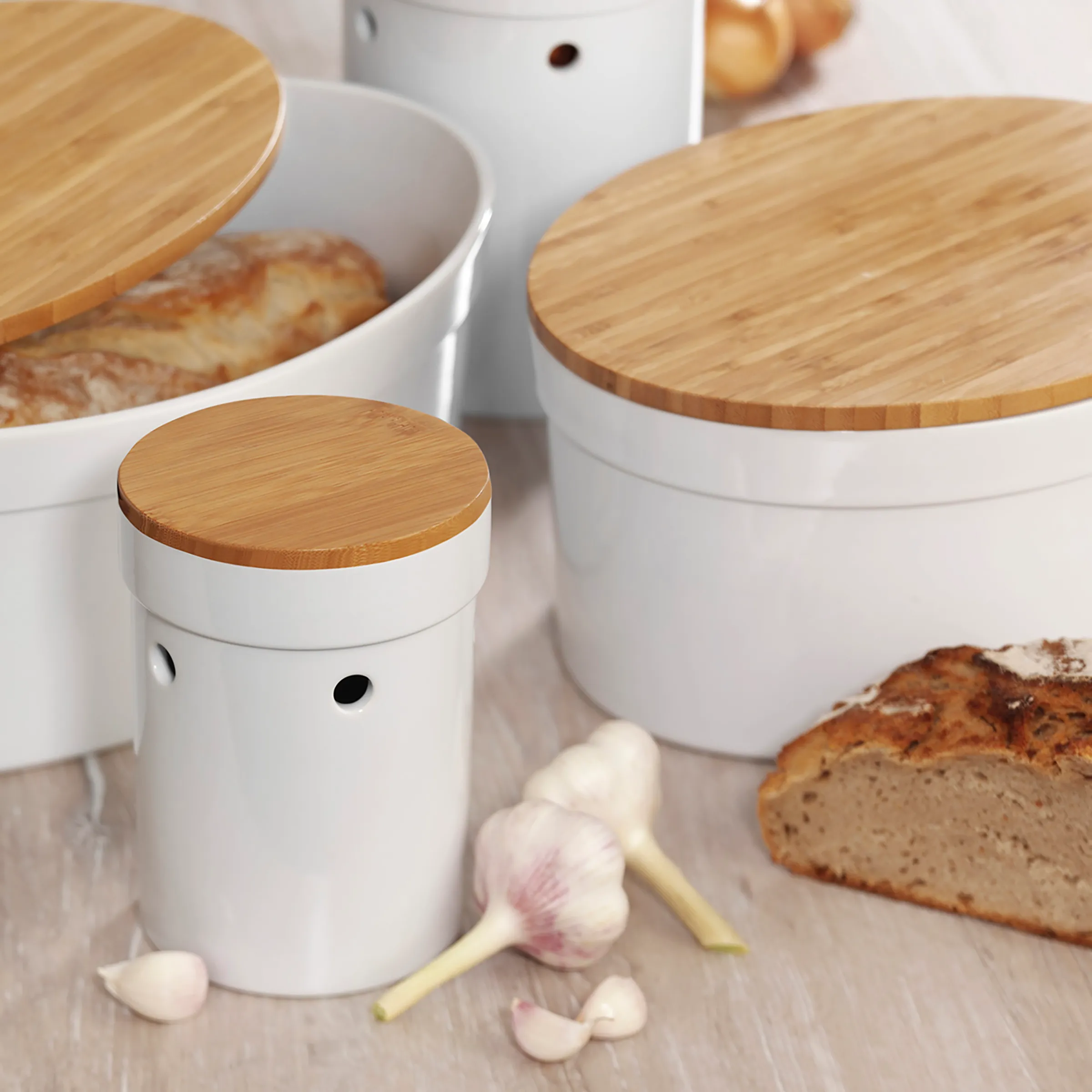 Weiße Vorratsdosen mit Bambusdeckel in drei Größen für Brot und Knoblauch auf Holztisch