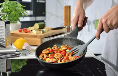Person cooking colorful vegetables in a frying pan on an induction cooktop in modern kitchen