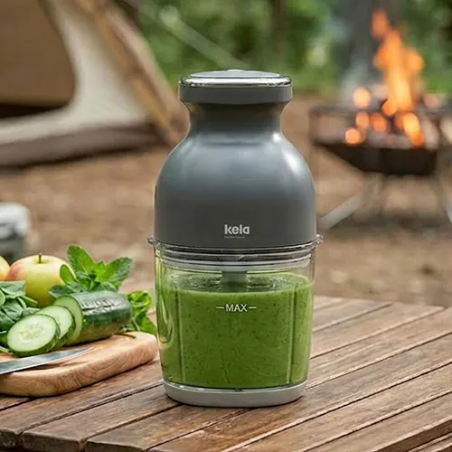 Kela Smoothie-Maker mit grünem Gemüsesaft auf Campingtisch vor Lagerfeuer
