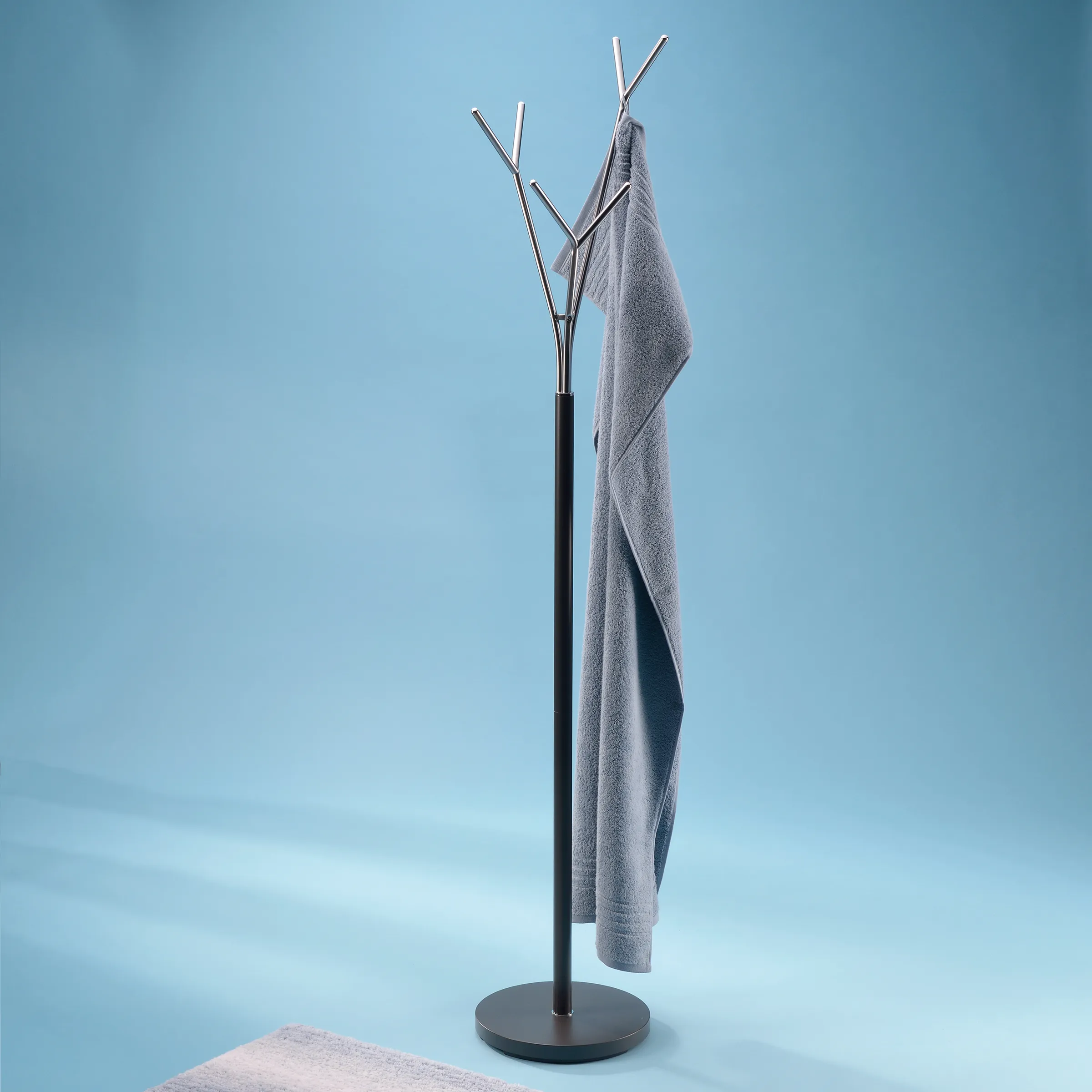 Garderobenständer mit Handtuchhalter - modernes Design Schwarzer Garderobenständer mit mehreren Metallhaken und einem grauen Handtuch, das daran hängt, auf blauem Hintergrund