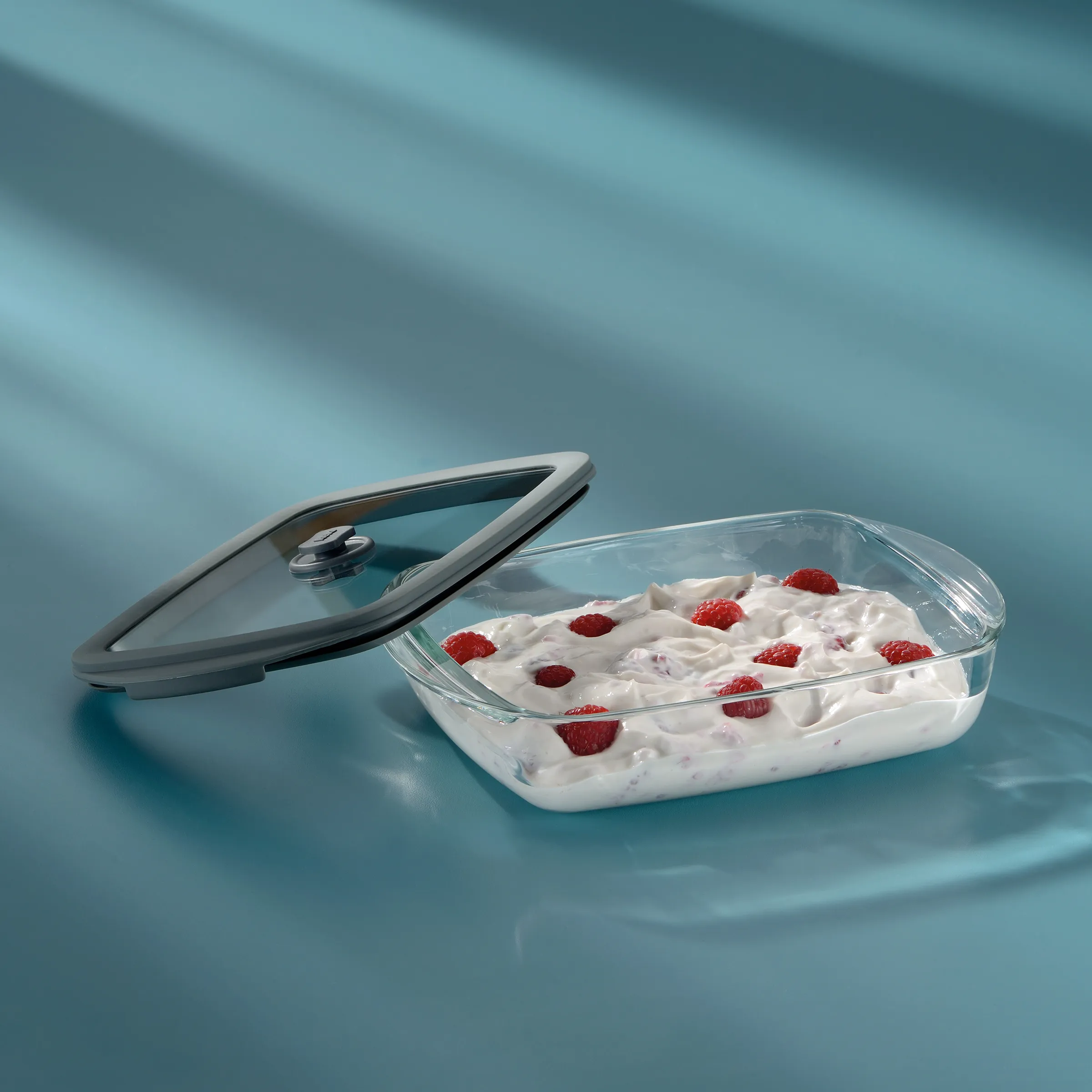 Glas-Frischhaltedose mit Deckel - Joghurt und Himbeeren Aufbewahrung Glas-Frischhaltedose mit Deckel gefüllt mit Joghurt und Himbeeren auf blauem Hintergrund