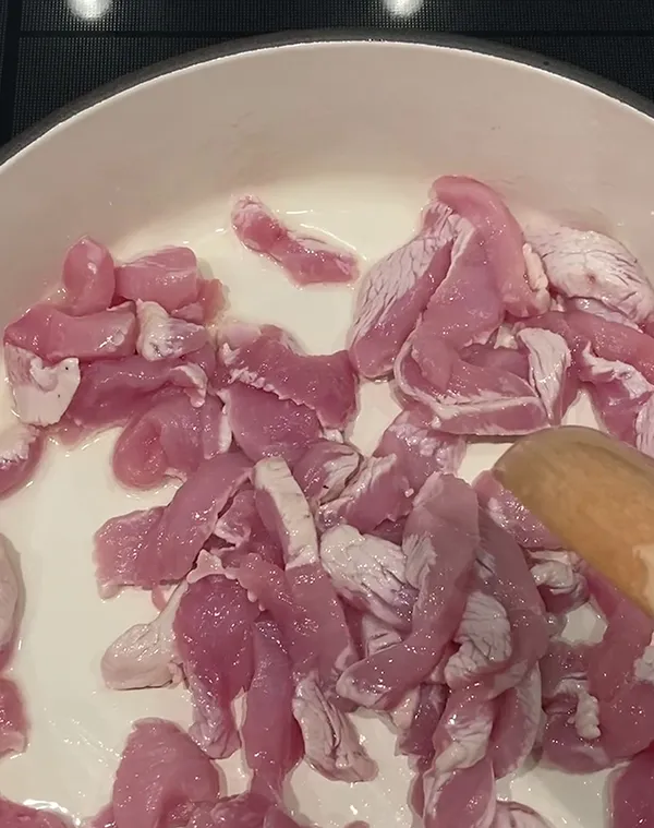 Rohe Hähnchenleber-Stücke in einer weißen Schüssel mit Milch, von oben fotografiert mit Holzlöffel.