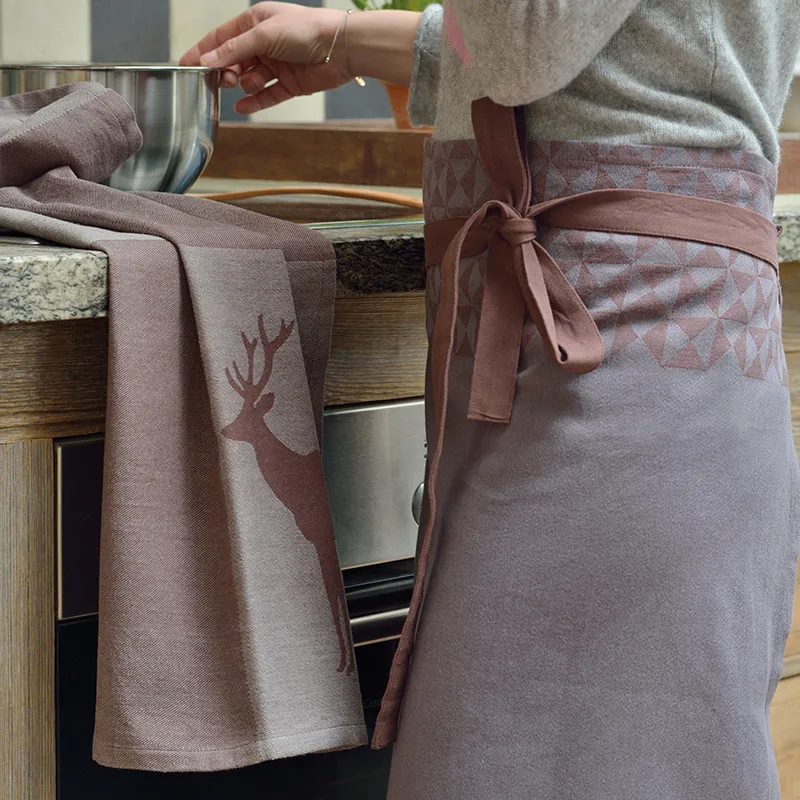 Ensemble Tablier de Cuisine et Torchon avec Motif Cerf Rose et Gris Personne en vêtements gris portant un tablier de cuisine rose à la cuisinière, torchon motif cerf à côté
