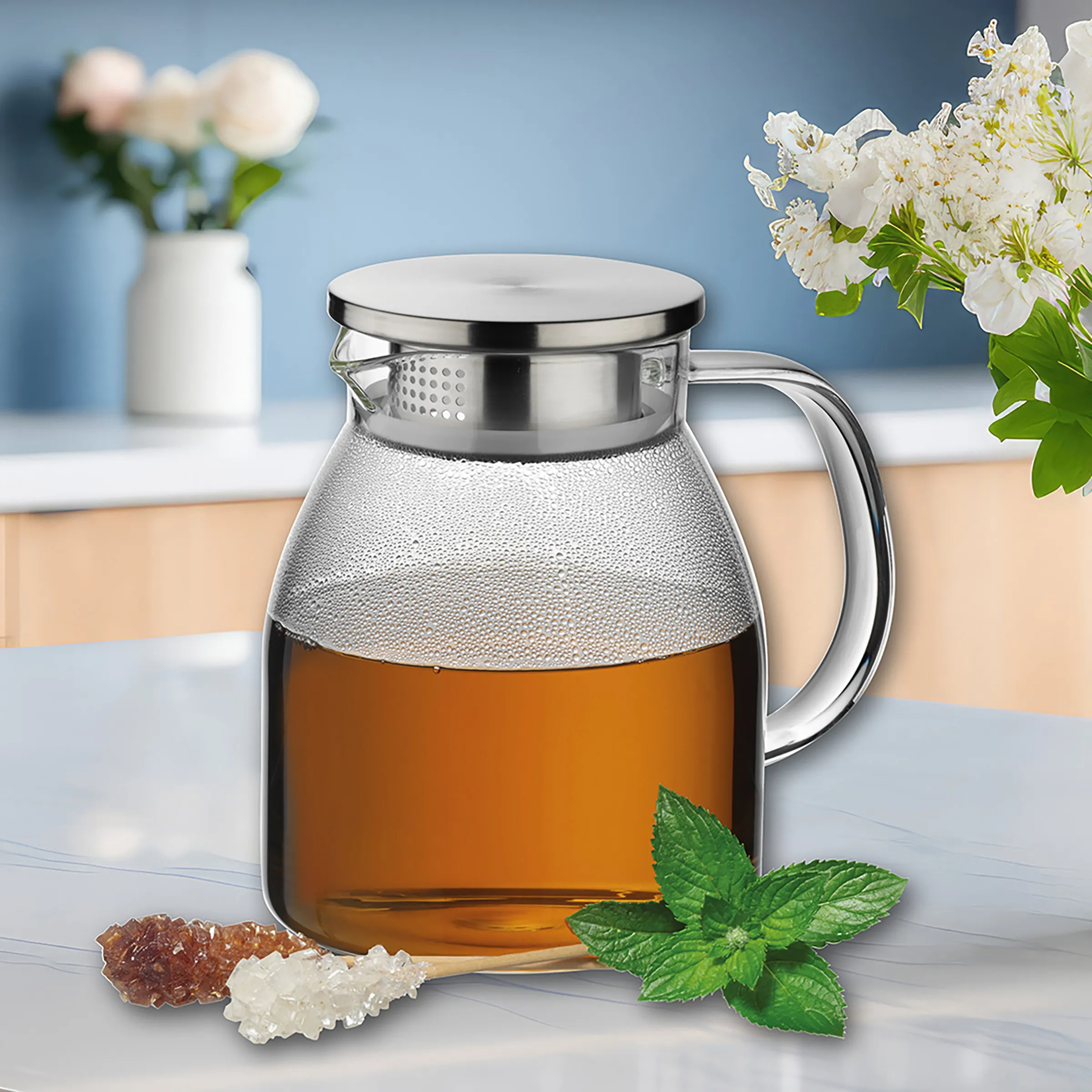 Teekanne Glas mit Sieb - hochwertiges Teeservice Glaskanne mit Tee und Metallsieb, umgeben von Minzblättern und Zuckerkristallen auf hellem Tisch