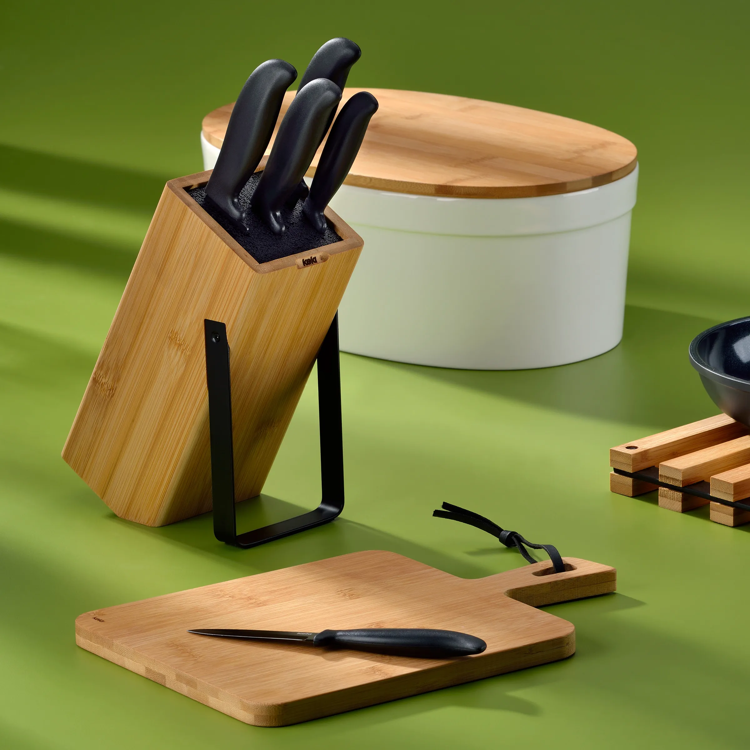 Bamboo-Messerblock mit schwarzen Messern und Holzschneidebrettern auf grünem Hintergrund