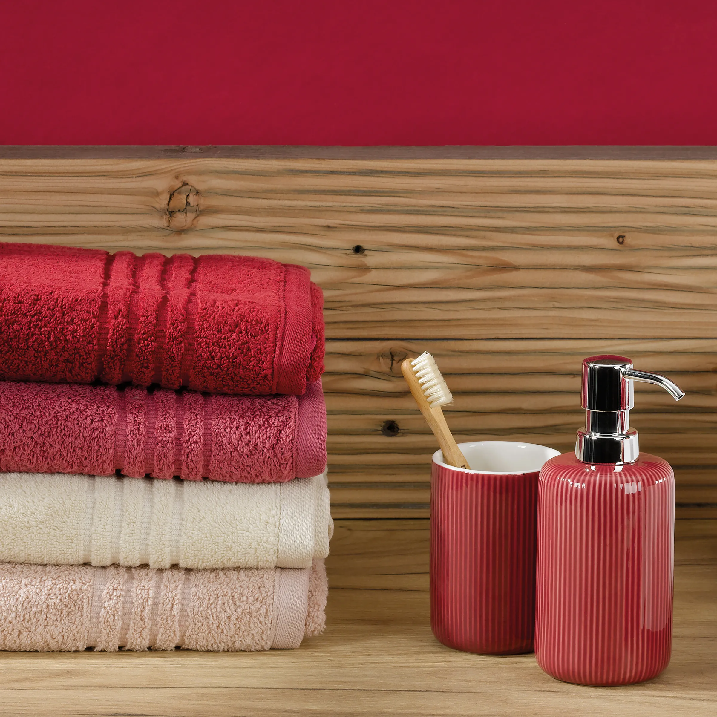 Badezimmer Handtücher Set mit Accessoires Rote Handtücher gestapelt neben roten Badaccessoires und Holzwand mit Zahnbürste und Seifenspender