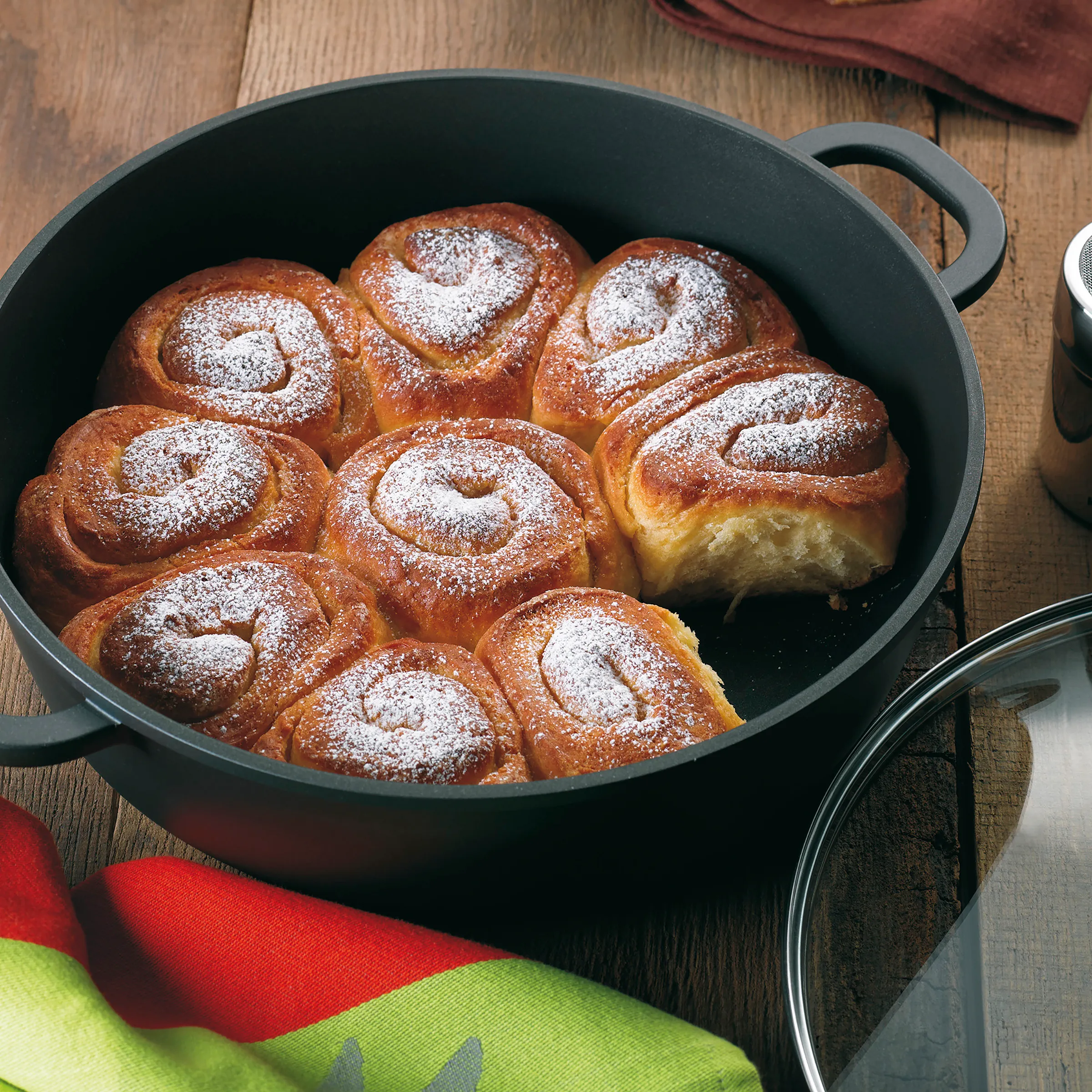 Zimtschnecken Rezept - Frische Backware im Gusseisen Neun frisch gebackene Zimtschnecken mit Puderzucker bestäubt in schwarzem Gusseisen-Bräter auf Holztisch