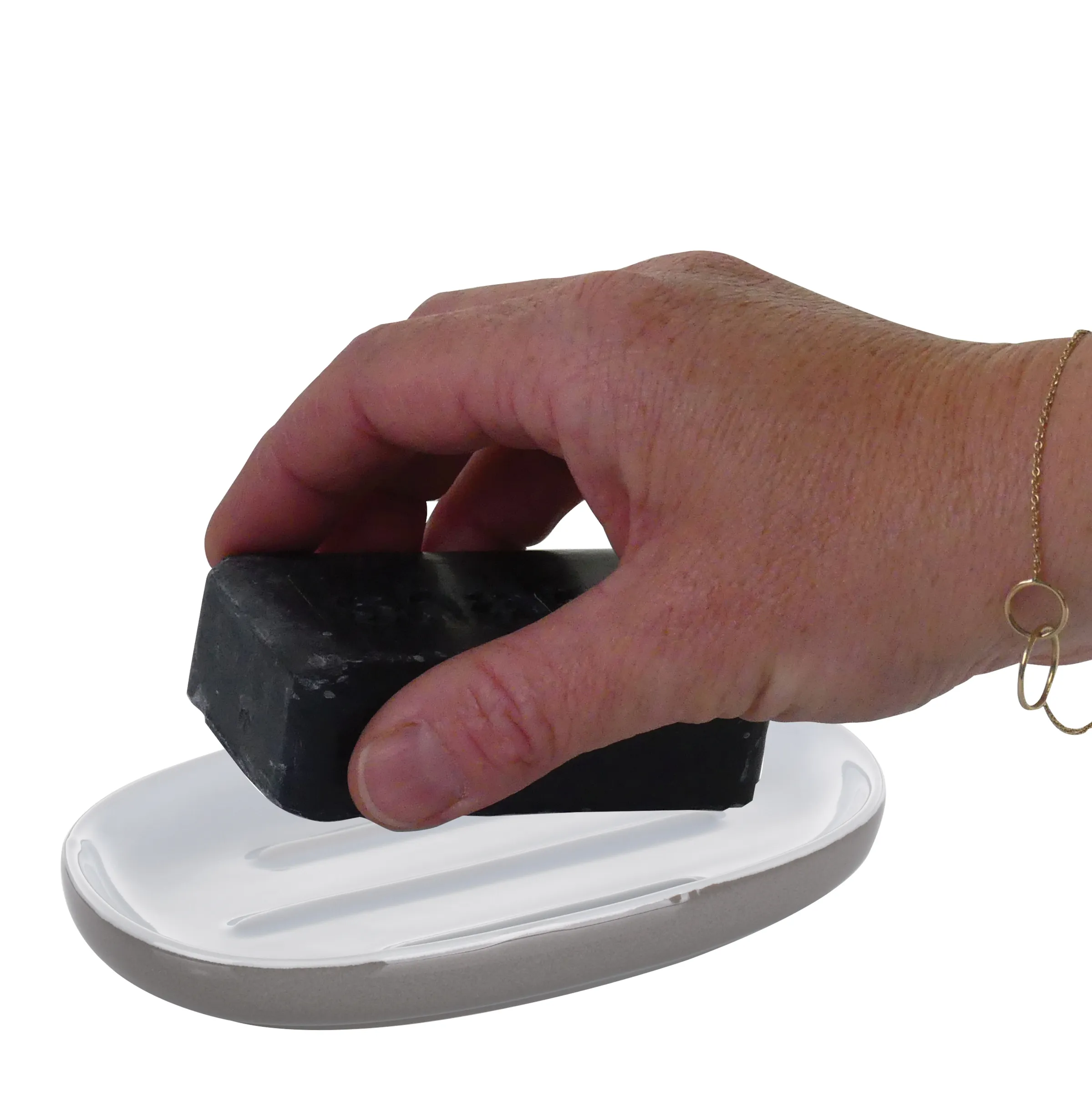 Schwarze Seife auf Seifenschale - Handgemachte Naturseife Hand formt schwarze Seife auf weißer Seifenschale, Armband sichtbar