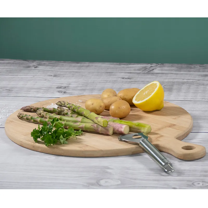 Frisches Gemüse auf Schneidebrett - Küchenzubehör Holzschneidebrett mit frischem Gemüse: Spargel, Kartoffeln, Petersilie, Zitrone und Schäler auf grauem Holztisch