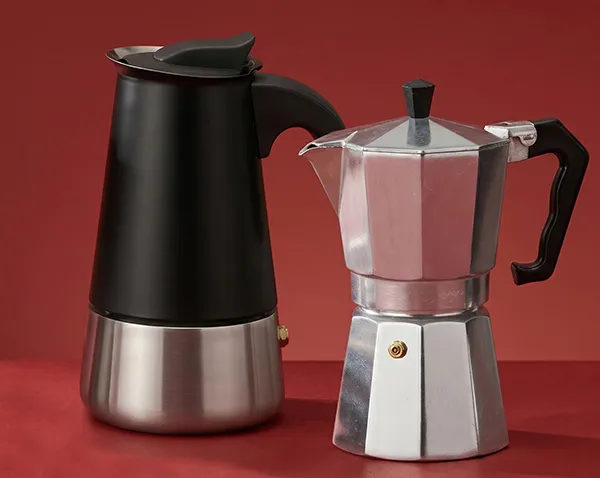Moderne schwarze Espressokanne und klassische silberne Mokakanne nebeneinander auf rotem Hintergrund
