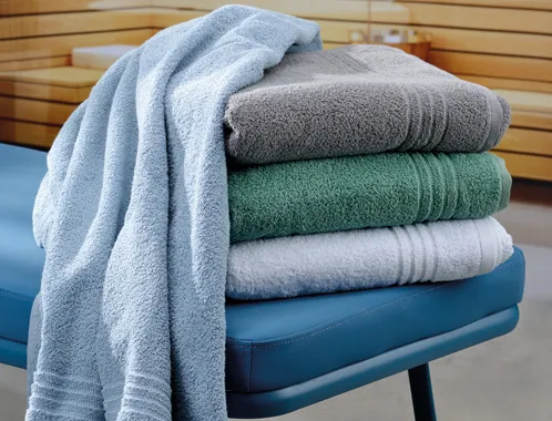 Stapel aus farbigen Handtüchern in Blau, Grau, Grün und Weiß auf einem blauen Stuhl mit hängendem hellblauem Handtuch
