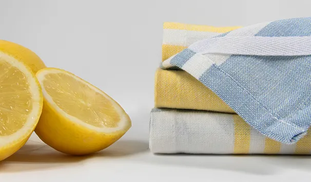 Zitrone und Geschirrtücher - Frische Küchenprodukte Halbierte Zitrone neben gestapelten Geschirrtüchern in Gelb, Blau und Weiß auf neutralem Hintergrund