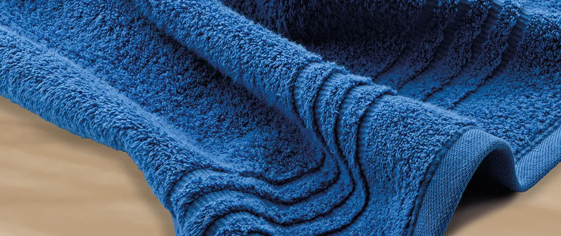 Gefaltete blaue Handtücher aus Frottee mit strukturierter Oberfläche, teilweise auf beigem Hintergrund