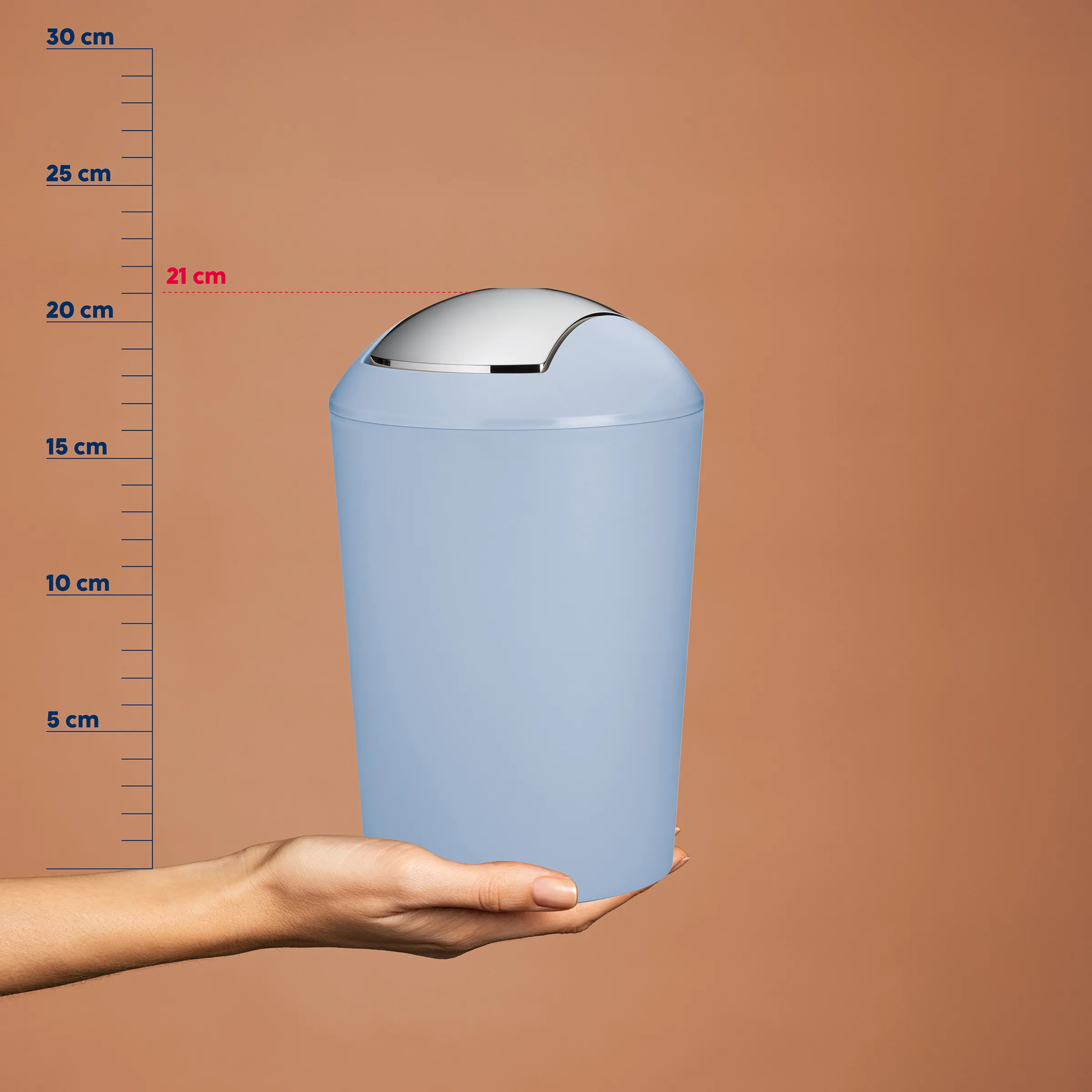 Sensor Abfalleimer 25 cm - Automatischer Mülleimer Blauer Abfalleimer mit Sensor-Deckel in der Hand, vor Zentimeter-Skala. Höhe etwa 25 cm.