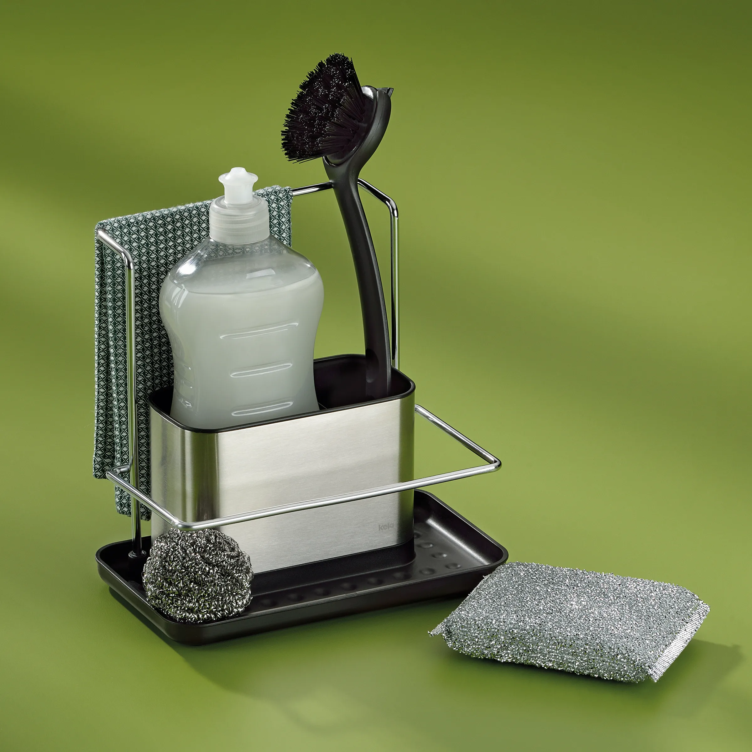 Spülbecken-Organizer Set mit Seifenspender und Spülbürste – Küchenhelfer Edelstahl Spülbecken-Organizer aus Edelstahl mit Seifenspender, Bürste, Schwamm und Spültuch vor grünem Hintergrund