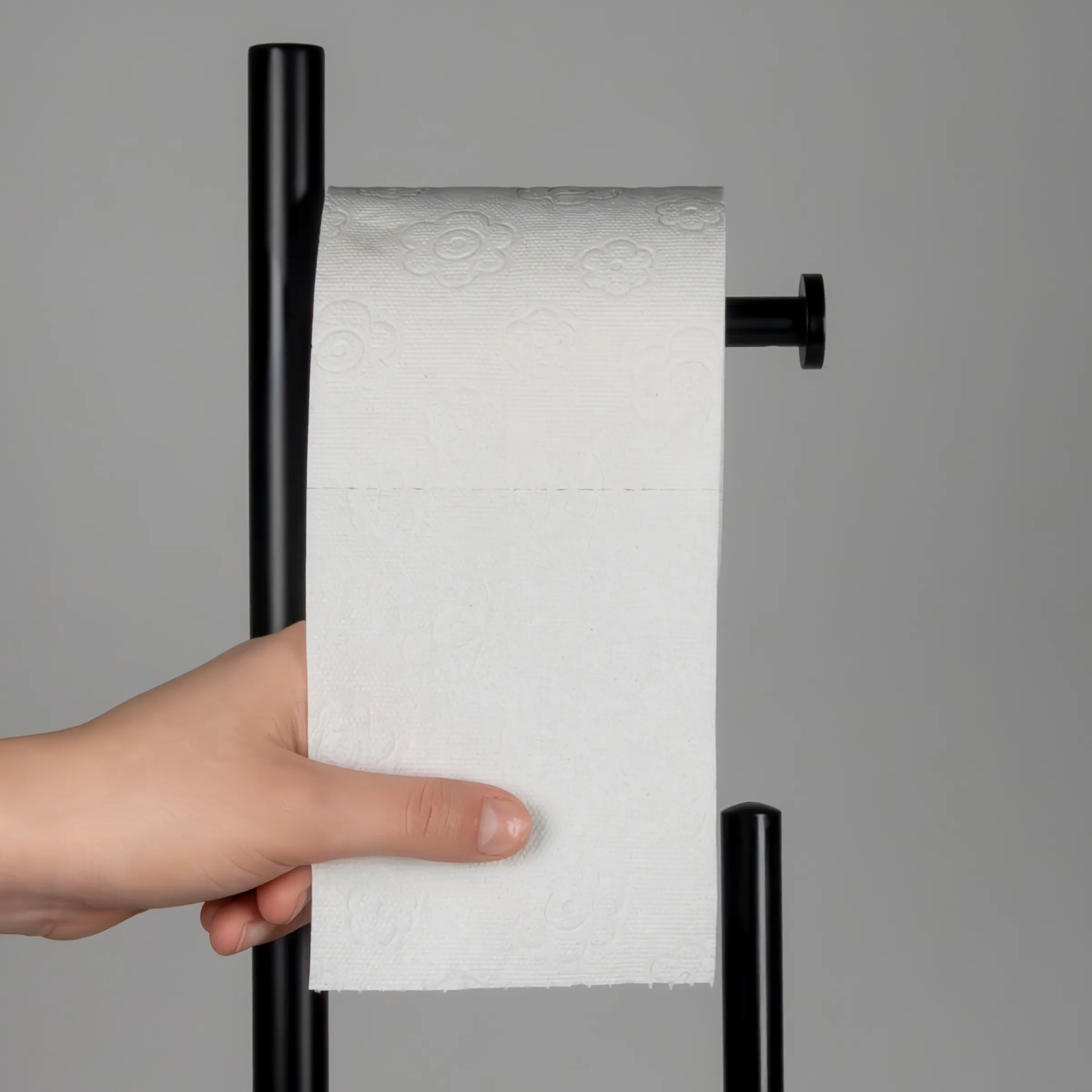 Schwarzer Küchenrollenhalter mit Toilettenpapier – moderne Wandmontage Hand zieht weißes Toilettenpapier von modernem schwarzem Küchenrollenhalter vor grauem Hintergrund