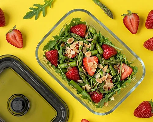 Frischer Rucola-Erdbeersalat mit Mandeln in Glasschale auf gelbem Hintergrund mit Erdbeeren und Spargel