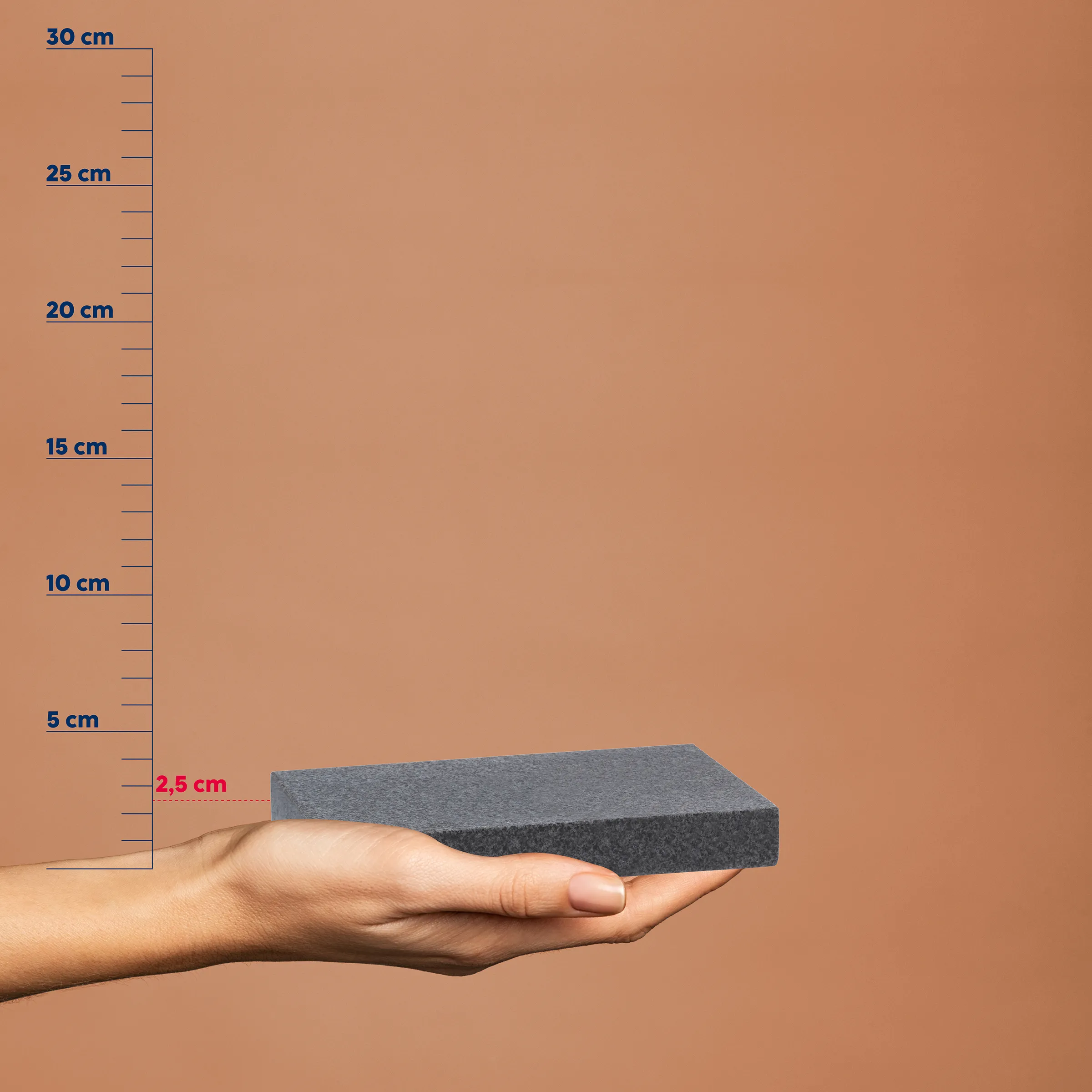 Hand hält grauen Schaumstoffblock vor Maßstab, Höhe 2,5 cm markiert