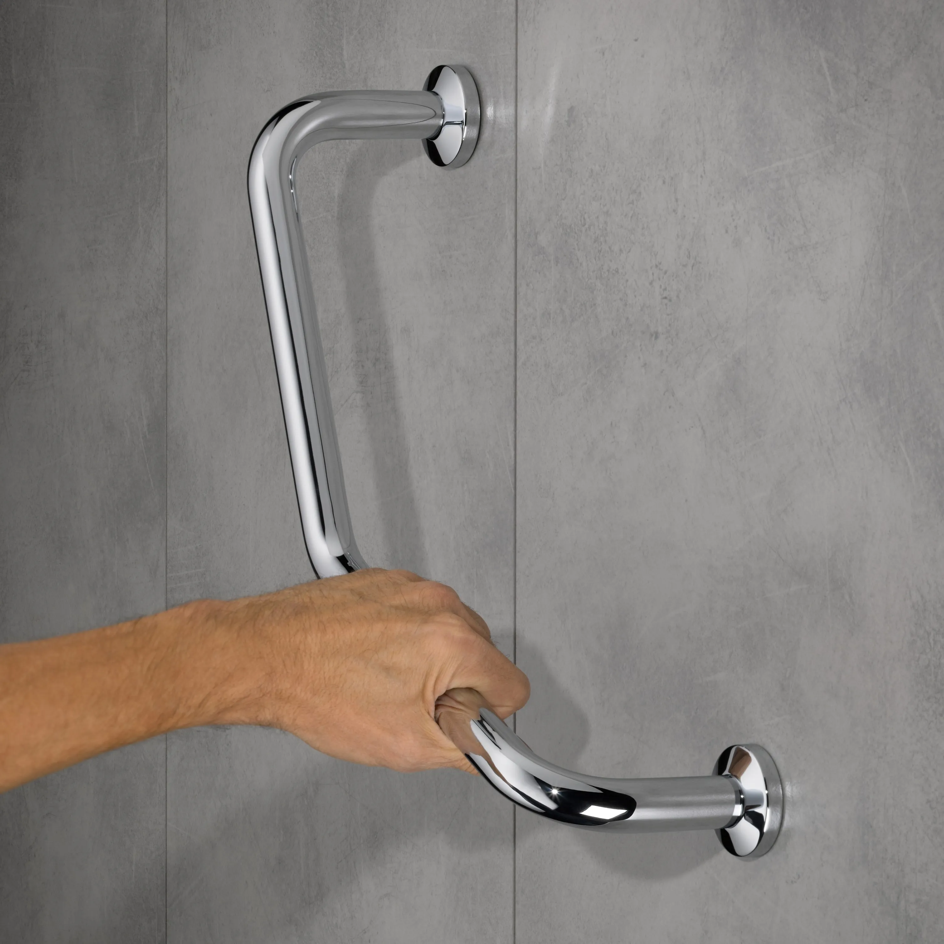 Barre de douche chromée avec deux poignées sur mur carrelé gris, une main saisit la poignée inférieure.