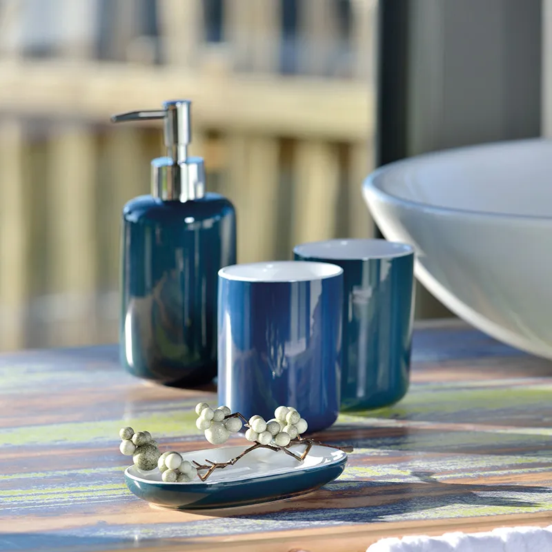 Badezimmer Accessoires Set blau - Moderne Badezimmer Deko Badezimmer-Accessoires-Set mit blauem Seifenspender, zwei Behältern und einer dekorativen Schale mit weißen Beeren auf Holzoberfläche.