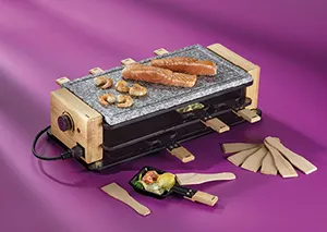 Raclette-Grill mit Natursteinplatte und Holz-Design - Raclette-Ofen für geselliges Kochen Raclette-Grill mit Holzgehäuse und Steinplatte, beladen mit Würstchen und Gemüse, mit Pfännchen vor lila Hintergrund