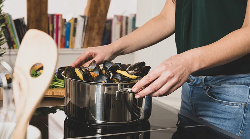 Muscheln kochen im Edelstahltopf - Induktionskochfeld Küche Person kocht Muscheln in einem Edelstahltopf auf einem Induktionskochfeld in moderner Küche