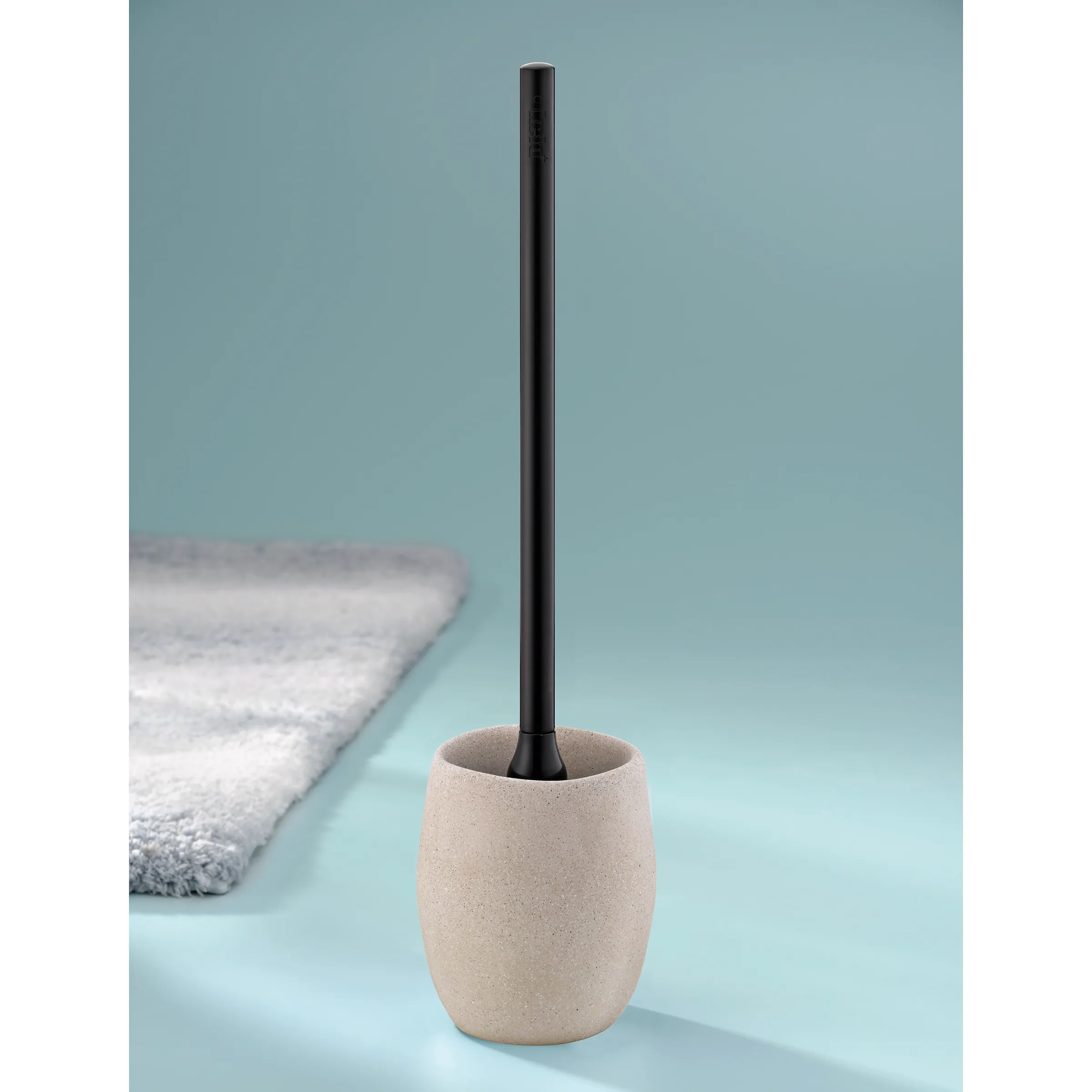 Toilettenbürste Betonoptik mit schwarzem Stiel Beige Toilettenbürste mit schwarzem Stiel in Betonoptik auf hellblauem Untergrund neben grauem Handtuch.