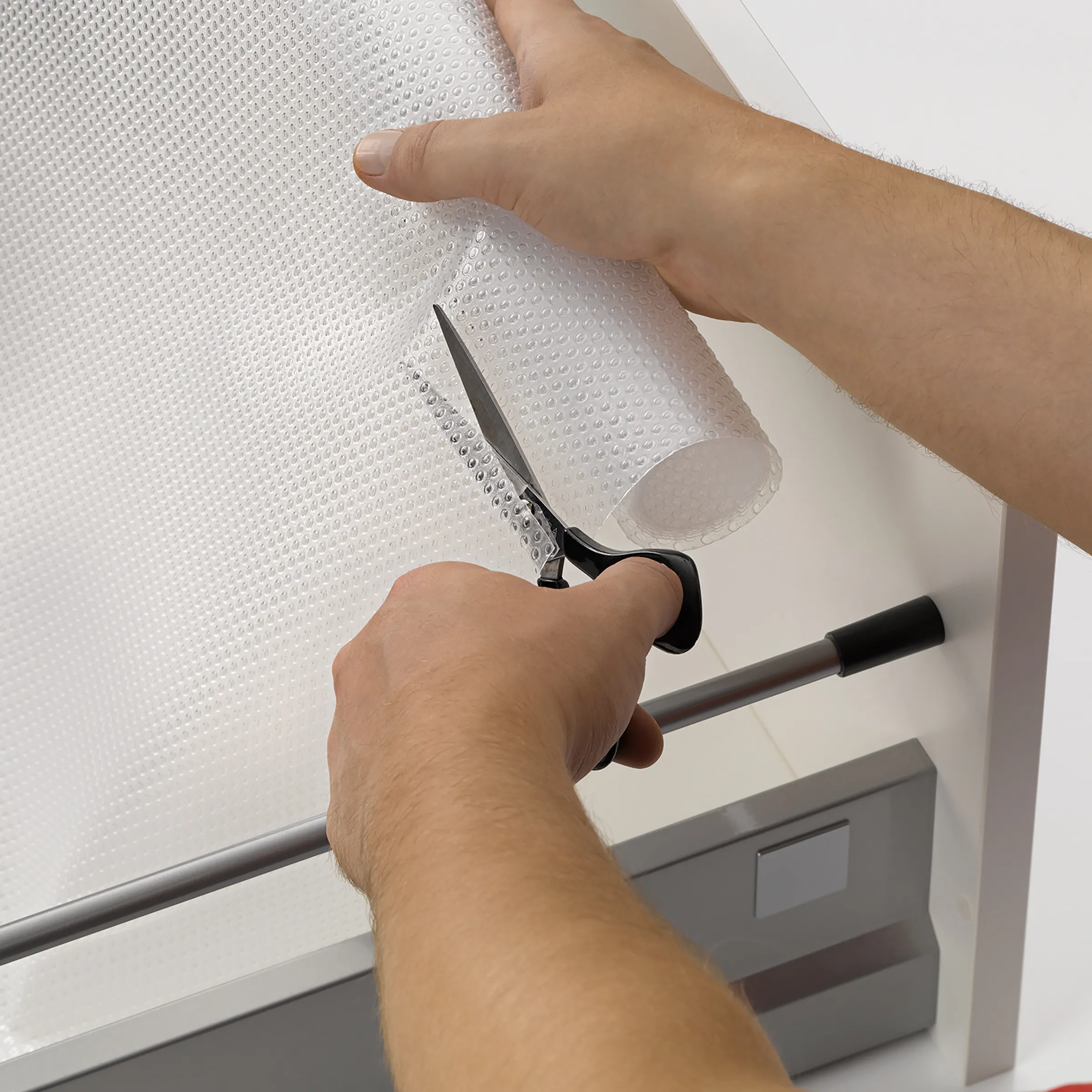 Hand schneidet Luftpolsterfolie mit Messer von einer Rolle ab