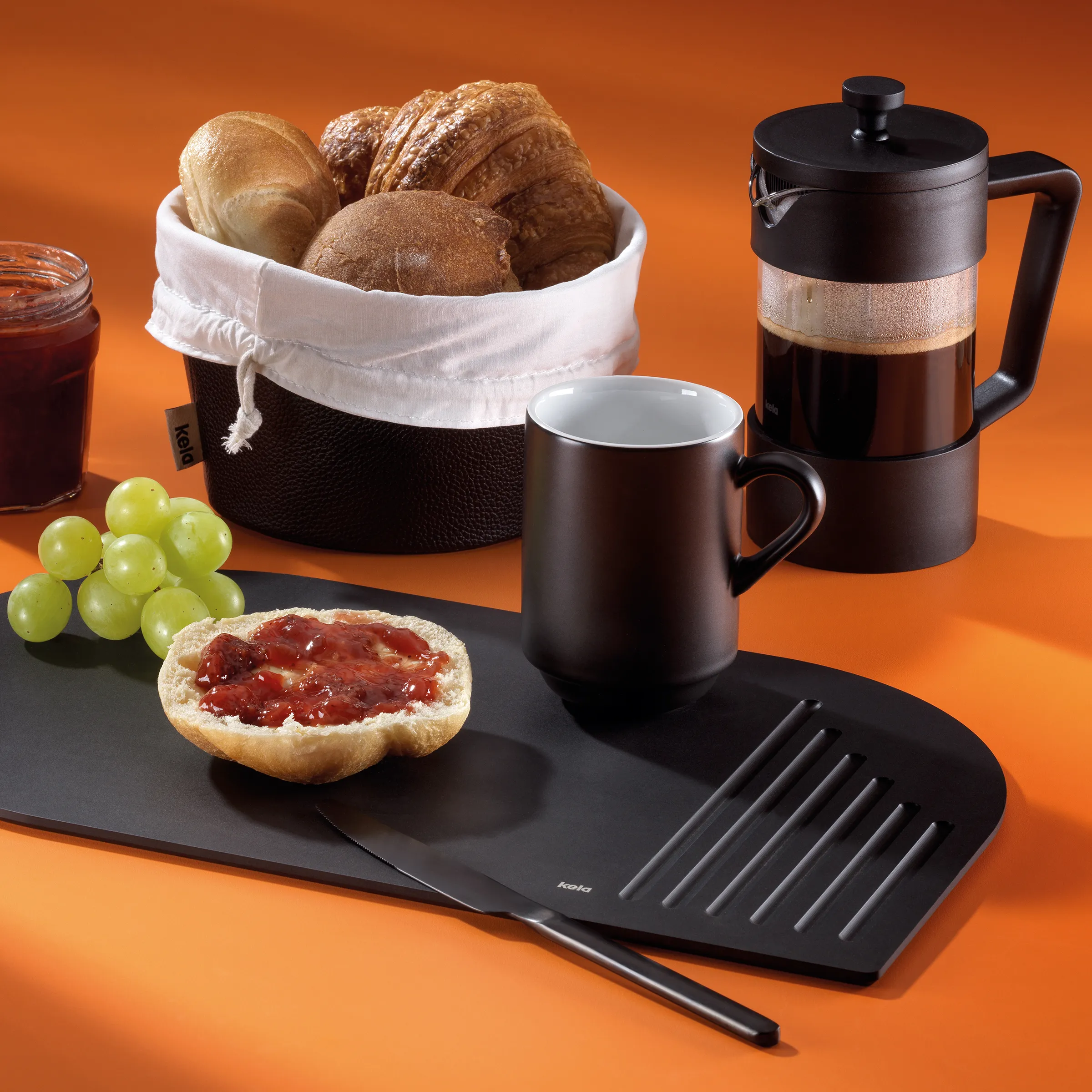 Frühstücks-Kaffee-Set mit Gebäck und Gebäckkorb Frühstücksset mit Kaffeekannenservice, Croissants, Brot, Marmelade auf Toast und grünen Trauben auf schwarzer Platte