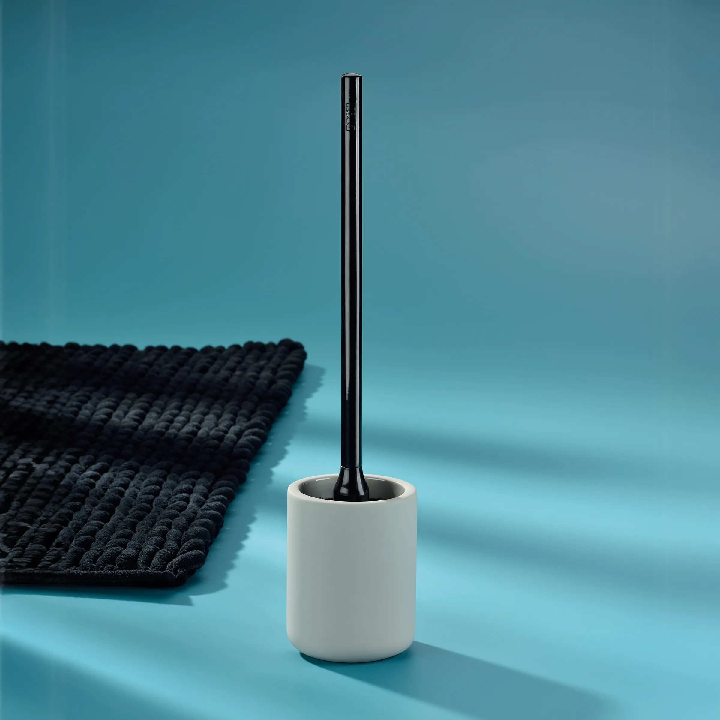 Moderne Toilettenbürste Keramik mit Halter Weiße Toilettenbürste mit schwarzem Stiel in weißem Keramikhalter auf blauem Hintergrund neben schwarzem Handtuch