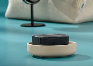 Schwarzer Seifenspender in beiger Keramikschale auf türkisfarbenem Untergrund mit Accessoires im Hintergrund