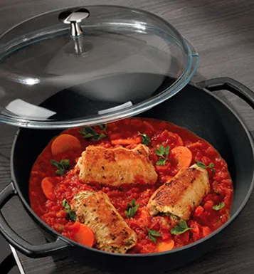 Chicken breast in red tomato sauce with bell peppers and herbs in black pot with glass lid