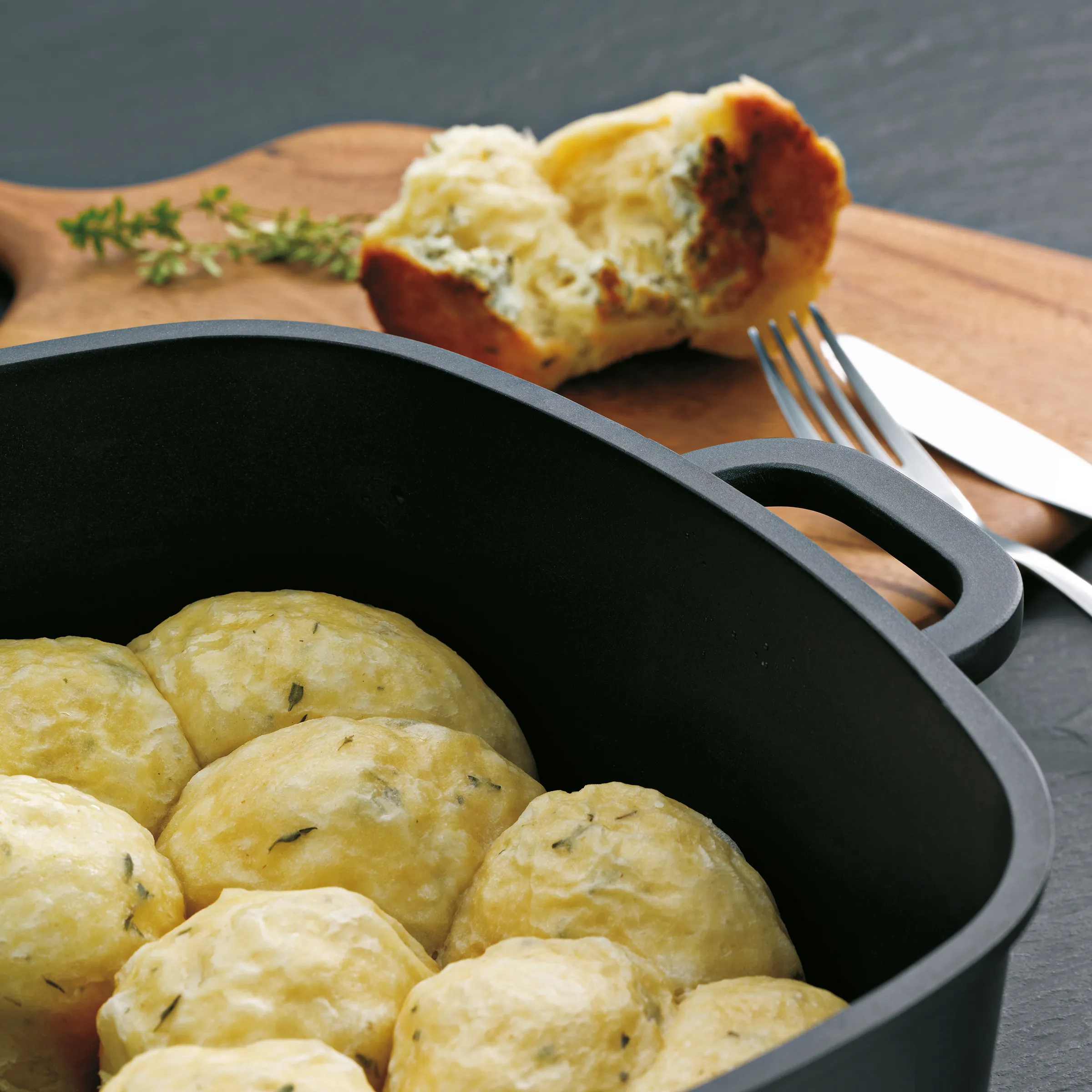 Semmelknödel in Pfanne - Traditionelle bayerische Knödel mit Kräutern Semmelknödel mit Kräutern in schwarzer Pfanne, aufgeschnittener Knödel auf Holzbrett mit Besteck