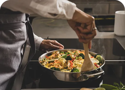 Professionelle Pasta-Zubereitung in der Gastronomie-Küche mit frischem Gemüse Koch rührt frische Pasta mit Gemüse in einer Edelstahlpfanne in professioneller Küche um